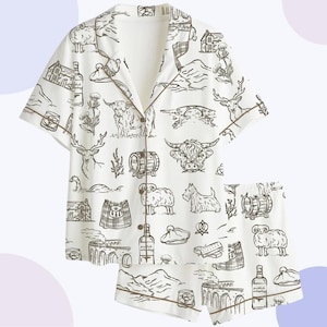 May include: White pajama set with a short-sleeved button-up shirt and shorts. The set features a repeating black and white illustrated pattern of Scottish landmarks, animals, and objects, including sheep, stags, and whiskey bottles.
