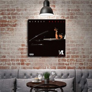 May include: A framed poster featuring the text "Nipsey Hussle" in red. The image shows a person in a car with their arm raised. The poster has a black background with the "VL Victory Lap" logo.