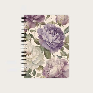 Könnte beinhalten: Ein spiralgebundenes Notizbuch mit floralem Design. Das Cover zeigt große Pfingstrosen im Aquarellstil in Lila-, Lavendel- und Cremetönen mit grünen Blättern auf cremefarbenem Hintergrund. Das Notizbuch hat eine schwarze Spiralbindung.