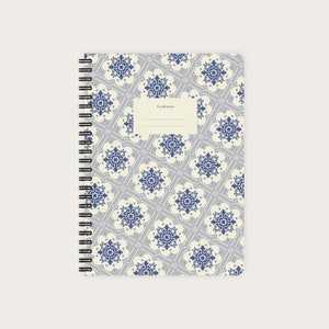 Op de afbeelding: Een wit spiraalnotitieblok met een blauwe en witte bedrukte omslag. De omslag heeft een herhalend geometrisch ontwerp met een label waarop "Caderno" staat.