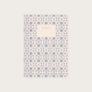 May include: A white notebook with a blue and white patterned cover. The cover has a label that says "NOTEBOOK".