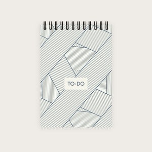 Könnte beinhalten: Ein weißes Spiralnotizbuch mit einem blauen und weißen geometrischen Muster auf dem Einband. Der Einband trägt den Text "TO-DO" in einem weißen Rechteck.