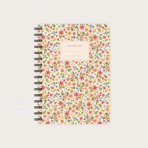 Könnte beinhalten: Ein spiralgebundenes Notizbuch mit floralem Muster. Der Einband hat einen cremefarbenen Hintergrund mit kleinen Blumen in Rot, Orange, Blau und Gelb. Ein rechteckiges Etikett in einem helleren Cremeton befindet sich in der Mitte, mit dem Wort "NOTEBOOK" darauf.
