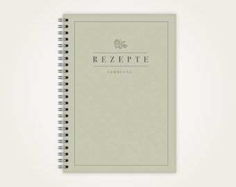 May include: A green spiral bound notebook with a dotted pattern and the text "REZEPT SAMMLUNG" in black. The notebook has a simple olive branch design on the cover.