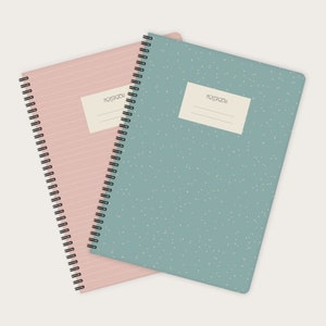 Könnte beinhalten: Zwei spiralgebundene Notizbücher, eines rosa mit horizontalen Linien und eines blau mit einem weißen, gesprenkelten Muster. Beide Notizbücher haben ein leeres Etikett mit der Aufschrift "Notebook" auf der Vorderseite.