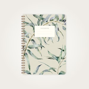 Könnte beinhalten: Ein beigefarbenes Notizbuch mit Spiralbindung und einem Aquarelldesign aus grünen Blättern. Der Einband hat den Schriftzug "NOTEBOOK" in Schwarz.