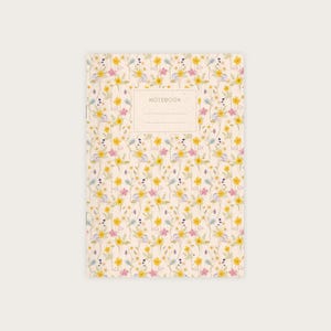 Könnte beinhalten: Ein Notizbuch mit einem Blumenmuster auf dem Einband. Der Einband ist hellbeige und zeigt verschiedene gelbe, rosa und violette Blumen. Das Wort "NOTEBOOK" ist in hellbrauner Farbe auf dem Einband gedruckt.