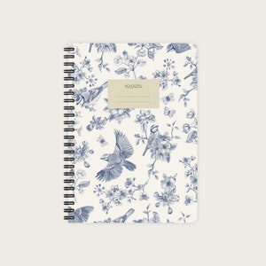 Könnte beinhalten: Ein weißes Notizbuch mit einem blauen und weißen Blumenmuster mit Vögeln und Schmetterlingen. Das Notizbuch hat eine Spiralbindung und das Wort "notebook" ist auf dem Einband aufgedruckt.