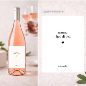 Könnte beinhalten: Eine Flasche Roséwein mit silbernem Verschluss und einem weißen Etikett mit dem Text "mama, i hob di lieb." und einem kleinen schwarzen Herz. Daneben eine weiße Karte mit demselben Text und einem schwarzen Herz.