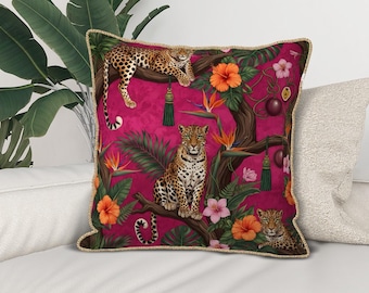 Puede incluir: Un cojín cuadrado decorativo con un fondo rosa vibrante que representa una escena de la jungla. El diseño incluye leopardos, flores de hibisco naranja y follaje verde. El cojín tiene un ribete dorado.