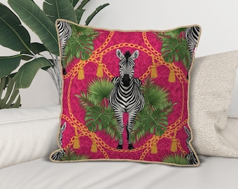 Op de afbeelding: Vierkant decoratief kussen met een levendige roze achtergrond met een zebra-illustratie, een gouden kettingontwerp en groene tropische bladeren. Het kussen heeft een gouden rand.
