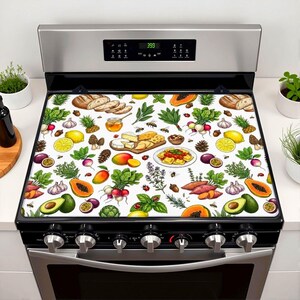May include: A white stove cover with a vibrant food illustration, including bread, fruits, vegetables, cheese, and honey. The design features lemons, avocados, radishes, and papaya. The cover is placed on a stainless steel cooker.