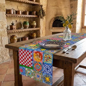 Könnte beinhalten: Ein rechteckiger Tischläufer mit einem lebendigen Patchwork aus bunten Fliesen im mediterranen Stil in Blau-, Gelb-, Rot- und Weißtönen, der auf einem Holztisch mit einem Keramikteller, einer Glasvase mit Zitronen und Besteck liegt.