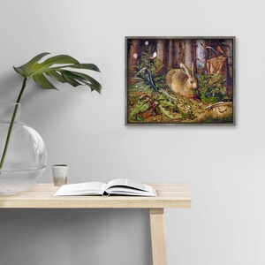 a painting of a rabbit in a forest setting, hanging on a wall above a wooden table with an open book and a glass vase.