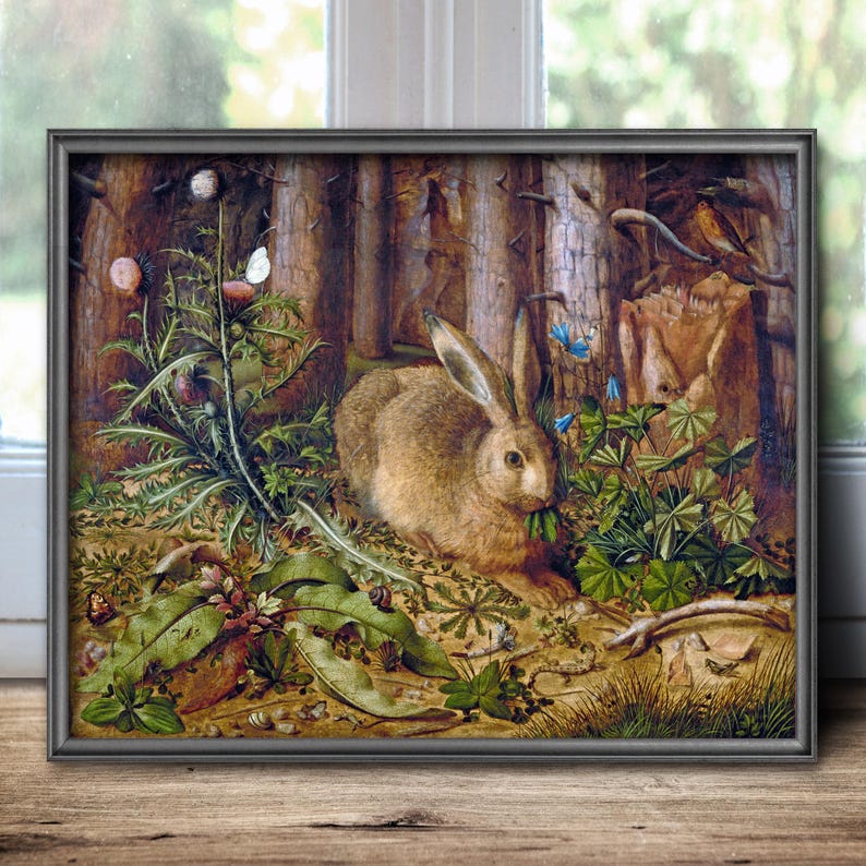 May include: A framed painting depicting a brown rabbit sitting in a forest clearing surrounded by green foliage, thistles, and small blue flowers. The scene includes a white butterfly, a small snail, and tree trunks in the background, all rendered in a detailed, naturalistic style with earthy tones.