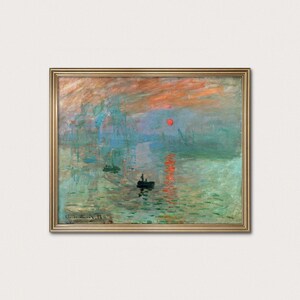 以下が含まれることがあります： 額縁に入った、海の風景画のプリント。この作品は、日の出時の港のシーンを描いており、背景にはボートや建物があります。空はオレンジ、赤、青の色合いが混ざり合い、水面には空の色が映し出されています。絵画は左下に署名されています。