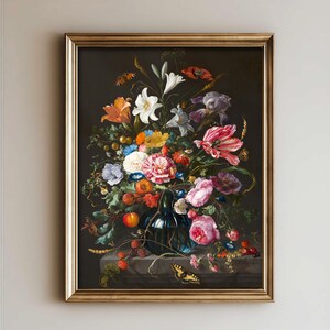 Op de afbeelding: Een ingelijst olieverfschilderij met een donker bloemstuk in een blauwe glazen vaas. Het boeket bevat witte lelies, roze rozen, oranje lelies en rode klaprozen, geaccentueerd door vlinders, kleine vruchten en korenaren op een stenen ondergrond.