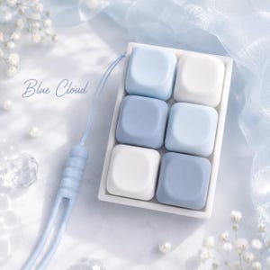 May include: A rectangular white tray containing six square, smooth-surfaced keycaps in varying shades of light blue and white. A light blue silicone strap with a ribbed connector is attached to the tray. The text Blue Cloud is visible.