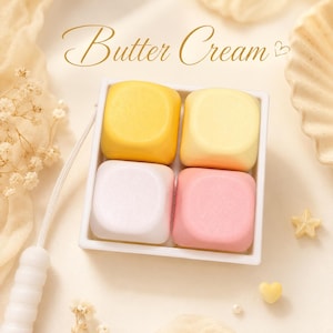 Könnte beinhalten: Ein quadratisches, weißes Tablett enthält vier farbige, würfelförmige Elemente: gelb, hellgelb, weiß und rosa. Die Worte "Butter Cream" sind in einer Schreibschrift geschrieben. Dekorative Elemente sind ein Stern und ein herzförmiges Objekt.