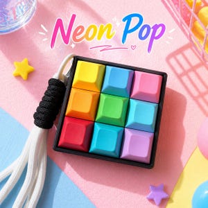 May include: A vibrant puzzle toy featuring a black frame and nine square buttons in rainbow hues. The text "Neon Pop" is displayed above the toy. A white cord with a black grip is attached. A fun, colourful toy.