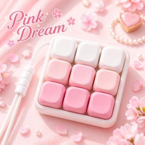 Peut inclure: Un pavé numérique mécanique carré à neuf touches avec un cadre blanc et un dégradé de neuf touches carrées allant du blanc au rose clair et au rose foncé. Le pavé possède un câble blanc et le texte Pink Dream écrit en lettres cursives roses.