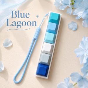 May include: A rectangular mechanical keyboard macro pad featuring five square keys in a gradient of blue, white, and gray tones. A light blue silicone wrist strap is attached to the top. The text Blue Lagoon is printed in dark blue on the left.