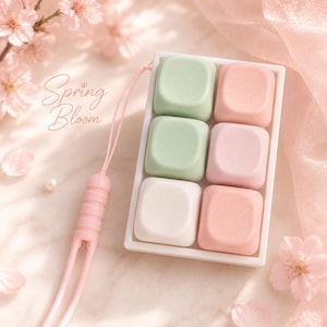 May include: A rectangular white tray containing six square, smooth-surfaced keys in pastel shades of green, pink, and white. A thin pink cord with a ribbed connector and a small white bead is attached to the side. The text Spring Bloom is visible.