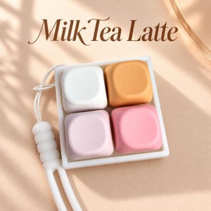 Può includere: Un vassoio quadrato bianco contenente quattro oggetti lisci di forma quadrata arrotondata in bianco, marrone chiaro, viola chiaro e rosa. Il vassoio è fissato a un cordino bianco con un manico testurizzato. Il testo Milk Tea Latte è stampato sopra.