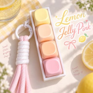 May include: A rectangular white frame containing four square keys in a gradient of yellow, peach, orange, and pink. A white plastic ring attaches to a pink cord tassel. Text on the image reads: Lemon Jelly Pink, Small Clicks Brighter Days, Sweet Little Things.
