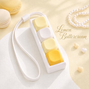 May include: A white rectangular mechanical keyboard switch tester with four square keycaps in shades of pale yellow, white, and bright yellow, attached to a white wrist lanyard. The text Lemon Buttercream is printed in cursive script.