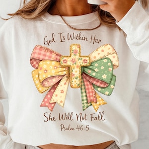 May include: White sweatshirt featuring a colorful bow and cross design. The bow has pink, yellow, and green sections with floral and plaid patterns. The text "God Is Within Her, She Will Not Fall, Psalm 46:5" is printed on the shirt.