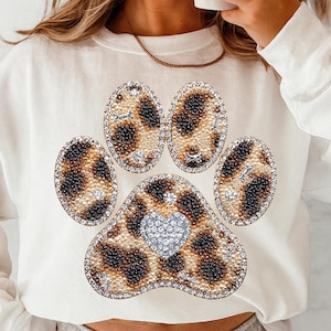 Può includere: Felpa color crema con un design a impronta di zampa tempestato di strass. L'impronta della zampa ha un motivo leopardato con un cuore al centro. L'impronta della zampa è delineata con strass e piccoli accenti di strass sono sparsi.