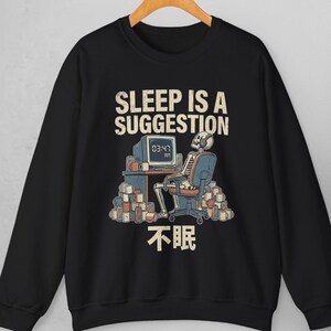 Puede incluir: Sudadera negra con un diseño gráfico de un esqueleto frente a una computadora. El texto "SLEEP IS A SUGGESTION" y caracteres chinos son visibles. La pantalla muestra "03:47 AM". El esqueleto está rodeado de pilas de libros.