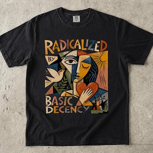 Könnte beinhalten: Ein schwarzes Kurzarm-T-Shirt mit einem farbenfrohen Grafikdruck im kubistischen Stil. Das Design zeigt ein stilisiertes Gesicht, eine weiße Taube, eine Sonne und ein Herz sowie den Text "RADICALIZED BY BASIC DECENCY" in fetter, bunter Schrift.