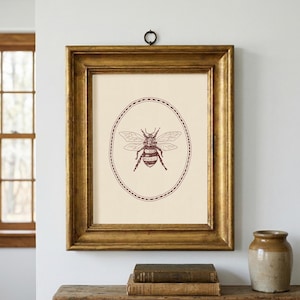 May include: A framed print featuring a detailed illustration of a bee within an oval border. The artwork is in shades of brown and cream, set in a gold-colored wooden frame. The print is hanging on a white wall.