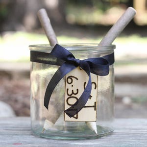 May include: A glass jar with a black ribbon and a wooden tag that says "S + T 6:30" with two wooden sticks inside.