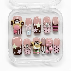 May include: A set of press-on nails in a clear plastic case. The nails feature various designs, including a monkey, stars, bows, skulls, polka dots, and stripes. Colors include pink, brown, white, and black. The nails are of various lengths and shapes.