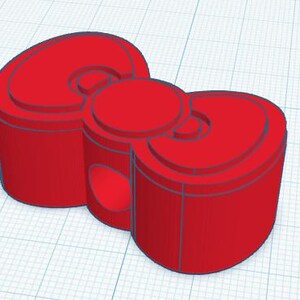 May include: A 3D-rendered red bow-shaped object. The bow has a cylindrical base with rounded edges and a circular center. The design includes layered details and a smooth, solid appearance. The object is set against a grid background.
