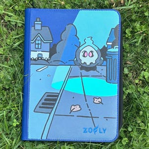 May include: A rectangular blue zippered binder featuring a graphic illustration of a small ghost-like character with pink eyes standing on a street at night near a house and a trash can, with the text ZOOFLY printed in blue at the bottom right.