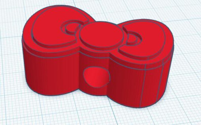 May include: A 3D-printed red bow-shaped object with a circular center and rounded edges. The bow has a layered design with a hollowed-out section on the bottom. The object is set against a grid background.
