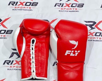May include: A pair of red boxing gloves with white accents. The gloves have a lace-up closure and the word "FLY" is printed on the front. The gloves are set against a backdrop with the text "RIXOB SPORTS BUILT FOR WARRIORS."