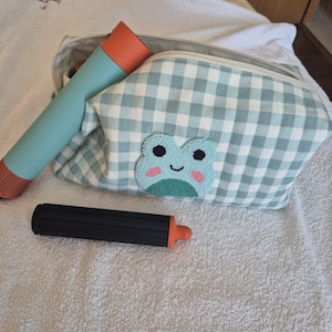 May include: A light blue and orange water bottle, a black and orange cylindrical object, and a blue and white gingham cosmetic bag with a frog applique. The bag is open, revealing the contents inside.