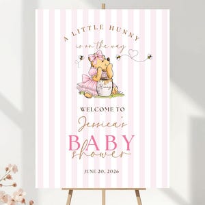May include: A vertical rectangular sign with a light pink and white vertical striped background. It features a cartoon bear wearing a pink dress and bow, sitting by a honey pot. Text reads: A LITTLE HUNNY is on the way, WELCOME TO Jessica's BABY SHOWER, JUNE 20, 2026.