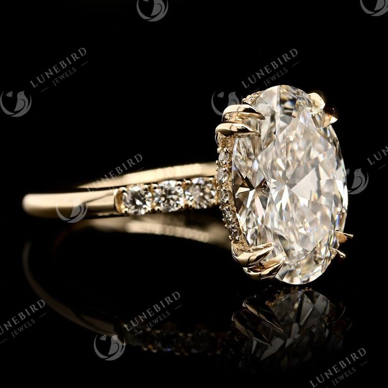 May include: A gold engagement ring featuring a large oval-cut diamond. The band is embellished with smaller diamonds. The ring is set against a black backdrop, accentuating its brilliance and design.