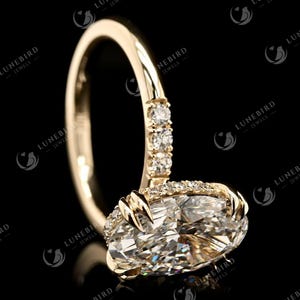 May include: A gold engagement ring featuring a large, oval-cut diamond. The band is polished gold, with smaller diamonds set along the band and around the main stone. The ring is displayed against a black backdrop.