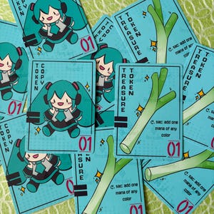 May include: A collection of rectangular game cards with a light blue background. Some cards feature a cartoon character with teal twin-tails, while others display a green leek illustration. Text includes COPY TOKEN, TREASURE TOKEN, and 01.