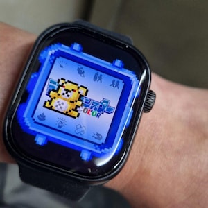 Könnte beinhalten: Schwarze Smartwatch mit einem pixeligen gelben Charakter auf einem blauen Bildschirm. Das Zifferblatt zeigt das Wort "COLOR" und andere pixelige Symbole. Die Uhr hat ein schwarzes Armband und einen schwarzen Knopf an der Seite.