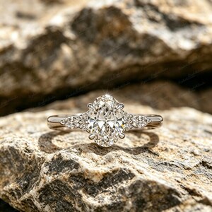 Op de afbeelding: Een zilverkleurige ring met een grote, centrale ovaal geslepen steen die door vier pootjes wordt vastgehouden. De band is aan weerszijden versierd met twee kleinere marquise geslepen stenen en een piepklein rond steentje in gepolijst metaal.