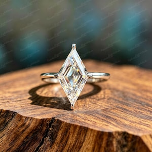 May include: A silver-toned ring featuring a large, clear, kite-shaped gemstone set in a prong setting. The band is smooth and metallic, supporting the elongated, faceted stone that tapers to points at the top and bottom, reflecting light clearly.