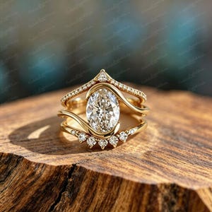 Puede incluir: Un conjunto de anillos de oro con una piedra central de corte ovalado rodeada por una banda curva con pequeñas piedras en pavé. El diseño incluye una sección superior puntiaguda y una banda inferior adornada con piedras redondas superpuestas.